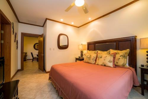 ein Schlafzimmer mit einem Bett mit orangefarbener Bettwäsche und Kissen in der Unterkunft Veranda 5A 1 bdr Garden View in Los Suenos in Herradura