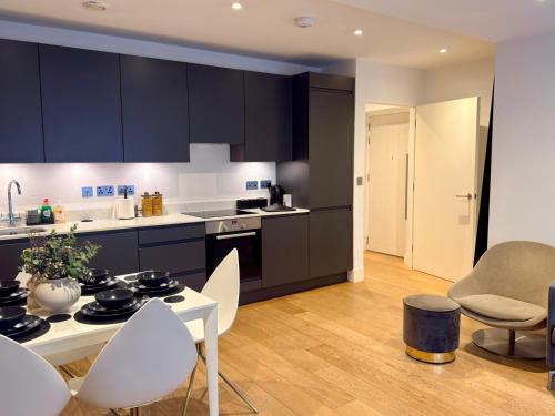 a kitchen with black cabinets and a white table and chairs at Modern & Luxurious 2-bed by ABBA, O2 & Canary Wharf in London