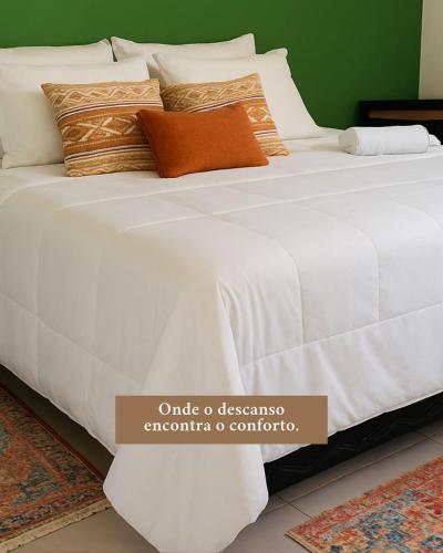 a bed with a white comforter and pillows at Sana Suítes in Macaé
