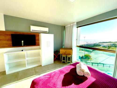 - une chambre avec un lit, une télévision et une grande fenêtre dans l'établissement Eu Amo Arraial Hospedagem - Studio Sophia I Vista Mar, à Arraial do Cabo