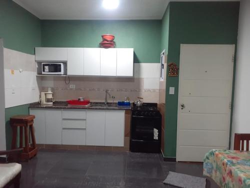 una cocina con armarios blancos y una pared verde en Departamento para 5 personas con pileta, en Villa Gesell