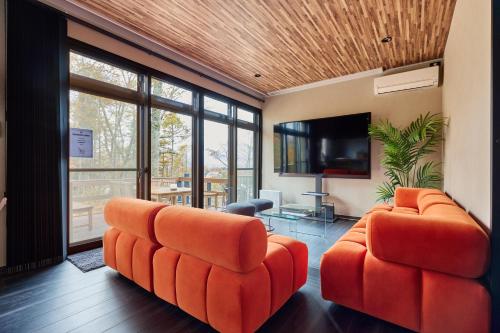 a living room with two orange chairs and a flat screen tv at 富士山を見ながらサウナBBQ The No10 MtFuji Forest House in Yamanakako
