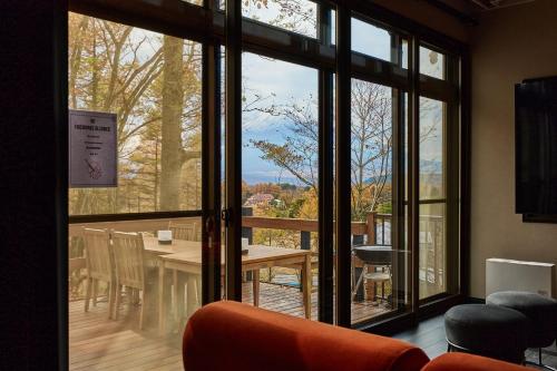 Una habitación con una gran ventana con una mesa y sillas. en 富士山を見ながらサウナBBQ The No10 MtFuji Forest House, en Yamanakako