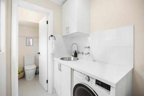 a white bathroom with a sink and a washing machine at Hazy Shores Escape - Breezy Coastal Stay near Henley Square in Henley Beach
