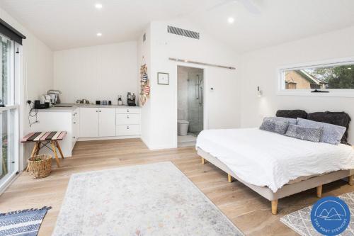 une chambre blanche avec un lit et une cuisine dans l'établissement Shoal Bay Beach House & Garden Suite - 200m to iconic beach, à Shoal Bay
