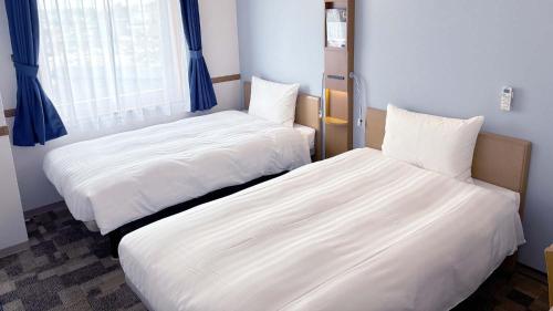 two beds in a small room with blue curtains at Toyoko Inn Hokkaido Tokachi Obihiro Ekimae in Obihiro