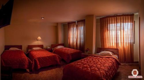 um quarto de hotel com três camas com cobertores vermelhos em Ebony Hotel em Huaraz