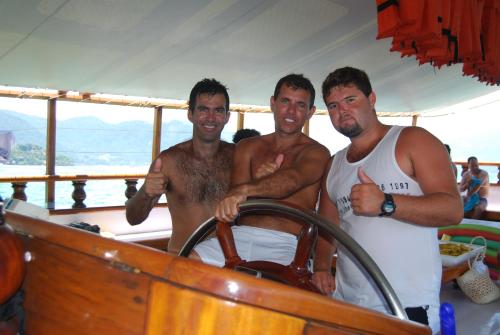 three men standing on a boat with a steering wheel at Pousada Agua Viva in Abraão