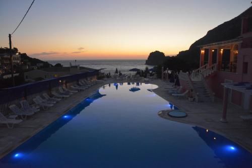 a swimming pool with chairs and the ocean at sunset at Hotel Elena Ermones in Ermones