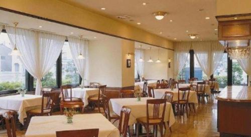 Un restaurante con mesas y sillas blancas y ventanas. en Hotel Harvest In Yonago, en Bakurōmachi