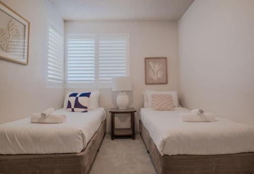 Dos camas en una habitación con paredes y ventanas blancas. en The Helm Unit 1 22 Voyager Close, en Nelson Bay