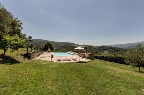 einen Pool mit Stühlen und einem Sonnenschirm auf einem Feld in der Unterkunft Freistehendes Agriturismo in der Toskana für sechs Personen mit großem gemeinschaftlich genutzten Garten und Pool in Pratovecchio