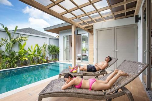 two women laying on chairs next to a swimming pool at Beach escape at Villa Dalaa 8 in Kamala Beach