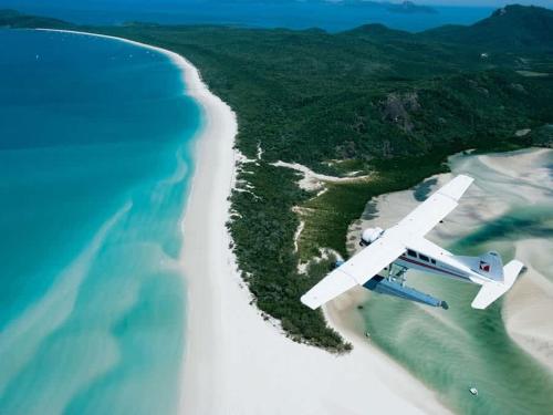 an airplane flying over a beach and the ocean at Coral Mango in Airlie Beach