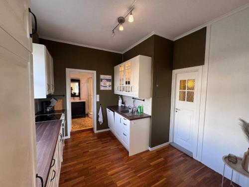 a kitchen with green walls and white cabinets and wooden floors at Brekkehagen in Skien