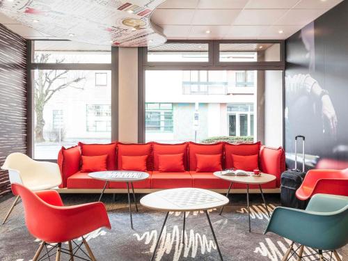 un canapé rouge dans une pièce avec des chaises et des tables dans l'établissement ibis Thonon Centre, à Thonon-les-Bains