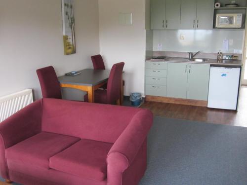 a living room with a red couch and a kitchen at The Bay Motel in Half-moon Bay