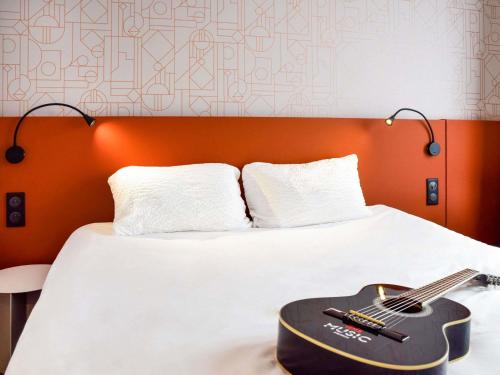 a guitar is sitting on a bed with a white sheet at ibis Rodez Centre in Rodez