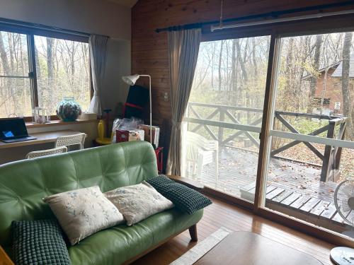 ein Wohnzimmer mit einem grünen Sofa und einem großen Fenster in der Unterkunft 森の中で仲間や家族とゆっくり過ごせる温泉付コテージ 会員制別荘地で広大なプライベート空間 ペット可 那須高原りんどうハウス in Nasu