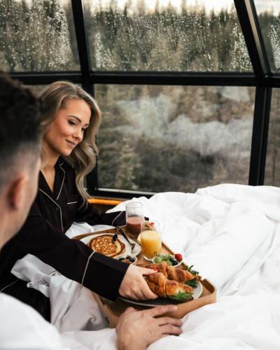 un uomo e una donna seduti a letto con un vassoio di cibo di SkyView Igloo Resort a Rovaniemi