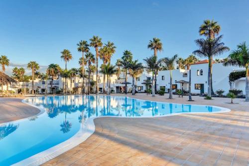 a swimming pool at a resort with palm trees and houses at Casa Oasis in Corralejo