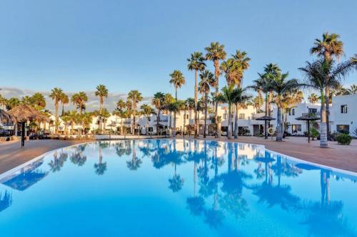 a large swimming pool with palm trees and buildings at Casa Oasis in Corralejo