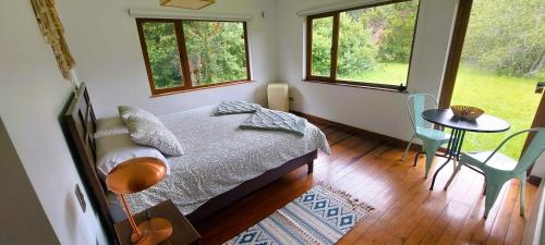 ein Schlafzimmer mit einem Bett und einem Tisch und zwei Fenstern in der Unterkunft Anahata Lodge, Alojamiento Tranquilo en Medio de la Naturaleza in Puerto Varas