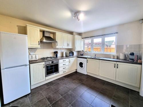 a kitchen with white cabinets and a white refrigerator at 3-Bedroom New Build House with Parking, Garden & Transport Links with Long Stay Offers in Thurcaston