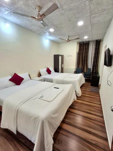 three beds in a room with white sheets and red pillows at Nagadeep Residency in Mysore