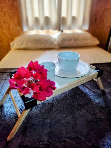 ein Tablett mit zwei Tassen und Blumen auf dem Bett in der Unterkunft Charmoso Chalé container em Piracaia, in Piracaia