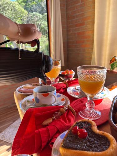 een persoon die sinaasappelsap in een beker giet op een tafel bij Refúgio com Hidro, Lareira, Café da Manhã e Vista da Natureza in Santo Antônio do Pinhal