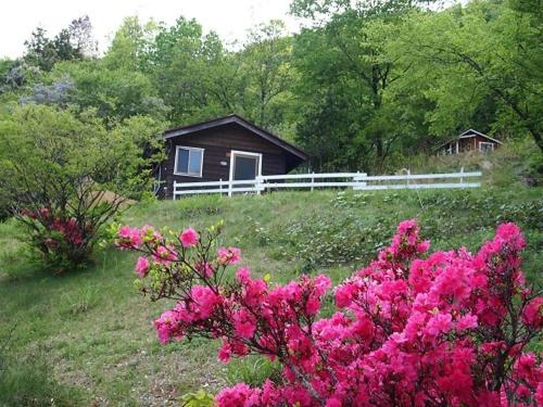 une maison avec une clôture blanche et des fleurs roses dans l'établissement Foresters Village Kobitto Southern Alps Camp Field - Vacation STAY 78099v, à Shirasu