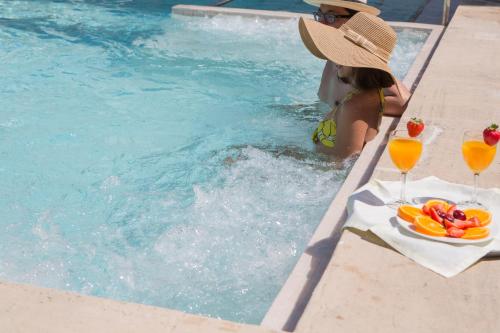 una mujer con sombrero sentada junto a una piscina con bebidas en L’Hermitage Hotel & Spa, en Orient