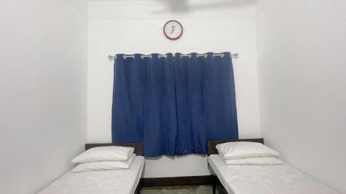 two beds in a room with a blue curtain and a clock at YMCA Girls Hostel, Mall Road, Lahore in Lahore
