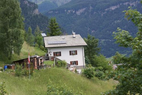 uma casa branca numa colina com montanhas ao fundo em Alpe Monte Massella em Poschiavo