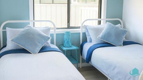 2 Betten mit Kissen neben einem Fenster in der Unterkunft Barefoot at Blacksmiths Beach in Blacksmiths