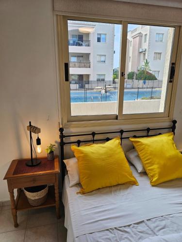 a bedroom with a bed with yellow pillows and a window at Front pool garden apartment in Paphos
