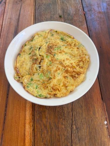een omelet in een witte kom op een houten tafel bij Petros Hostel in Nongkhiaw