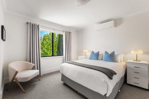 ein weißes Schlafzimmer mit einem Bett, einem Stuhl und einem Fenster in der Unterkunft Acorn Delight - Tranquil Retreat by the Golf Course in Dunsborough