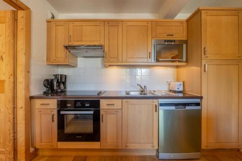 a kitchen with wooden cabinets and a stove and a sink at l'Ours Bleu C21 - Ski In Ski Out - Happy Rentals in Vallorcine