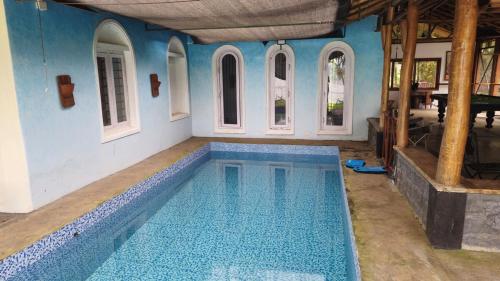 une grande piscine dans une maison aux murs bleus dans l'établissement Grace Backwater Villa Coorg, à Suntikoppa