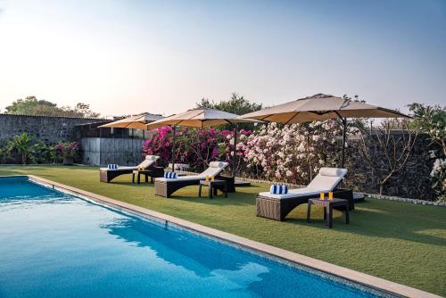 a group of chairs and umbrellas next to a pool at SaffronStays Brunton House - 3BR Villa with Pool & Alfresco dining in Alibaug