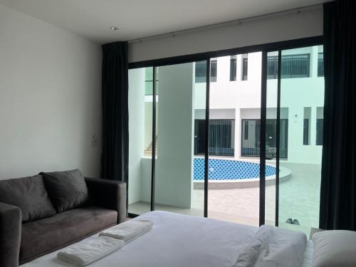 a bedroom with a bed and a couch and a large window at J&P Hotel Sriracha in Ban Hua Na
