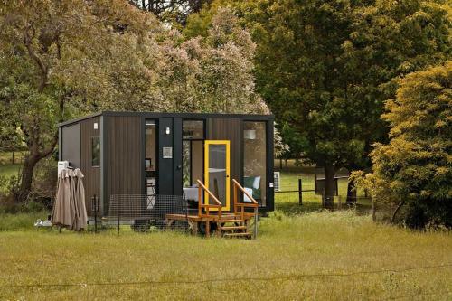 a black tiny house in a field with trees at Lazy Daisy Farm by Tiny Away in Warragul