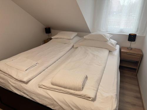 ein Bett mit weißer Bettwäsche und Kissen sowie einem Fenster in der Unterkunft Napfény Apartman in Marcali