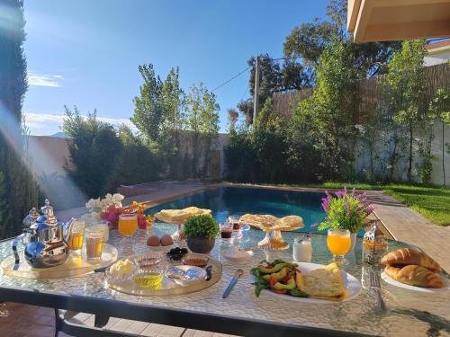 une table avec de la nourriture et des boissons à côté d'une piscine dans l'établissement Suite nature montagne et petit déjeuner Villa Fatima, à Fès