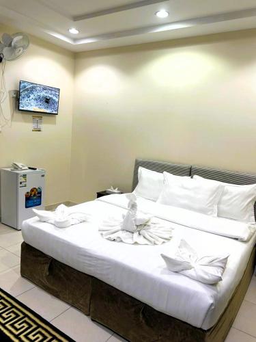 een groot bed met witte lakens en een tv aan de muur bij فندق منازل الحجاز شقق وغرف فندقية in Al ‘Azīzīyah