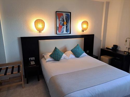 um quarto com uma grande cama branca com travesseiros azuis em Hôtel Le Collier em Antibes