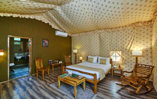 ein Schlafzimmer mit einem Bett und zwei Stühlen und einem Tisch in der Unterkunft WelcomHeritage Jungle Home Pench in Khawāsa