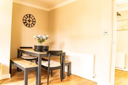 a dining room table and chairs with a clock on the wall at Stunning 5 Bedroom House in London - Sleeps up to 10 guests - Business - Contractors - Families - Leisure - WiFi - Parking - Garden in Grove Park